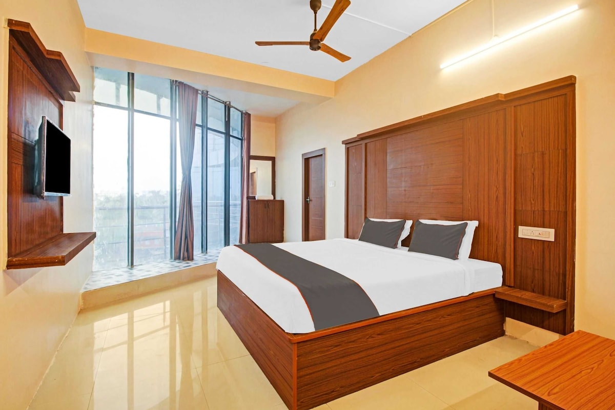 A modern bedroom with a large bed, wooden headboard, a ceiling fan, and a TV mounted on the wall.