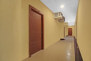 Un pasillo con puertas de madera, piso de baldosas y un equipo de aire acondicionado en la pared.