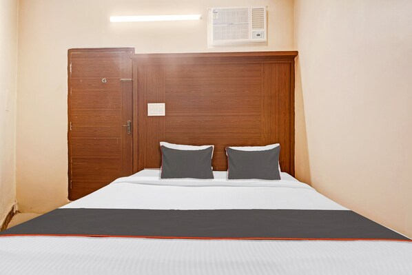 A bedroom with a wooden wardrobe, a bed with white bedding, two pillows, and a bedside table.