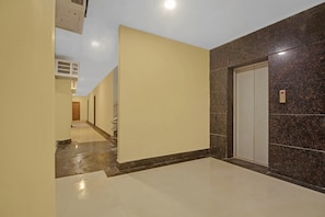 A corridor with a marble floor, a door with a control panel, and a wall with a textured pattern. - Collection O Hotel Aqua Villa Near (Kolkata)