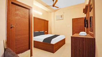 Habitación de hotel con cama y armario de madera, ventilador de techo y ventana pequeña con unidad de aire acondicionado.