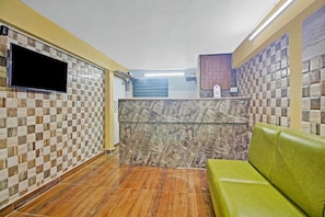 A reception area with a checkered tile wall, a marble reception desk, a green sofa, and a flat-screen TV mounted on the wall. - Collection O Hotel Aqua Villa Near (Kolkata)