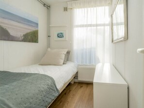 A bedroom with a bed, a radiator, a window with sheer curtains, and a painting on the wall. - Holiday Home in Renesse With Swimming Pool (Renesse)