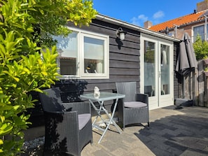 A patio with two wicker chairs and a small table, a glass door, and a window with a white frame. - Do27 Holiday Apartment Near the Center and Beach (Domburg)