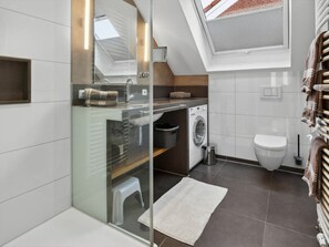 A modern bathroom with a glass-enclosed shower, a washing machine, and a toilet. - Lehmann House, Souther Stuuv (Norderney)