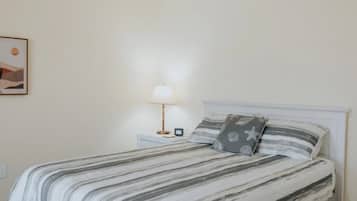 Quarto com cama, mesa de cabeceira com abajur e quadro na parede.