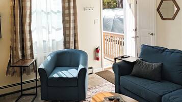Una sala de estar con un sillón azul, un sofá azul, una mesita con un cuenco y un tapete estampado.