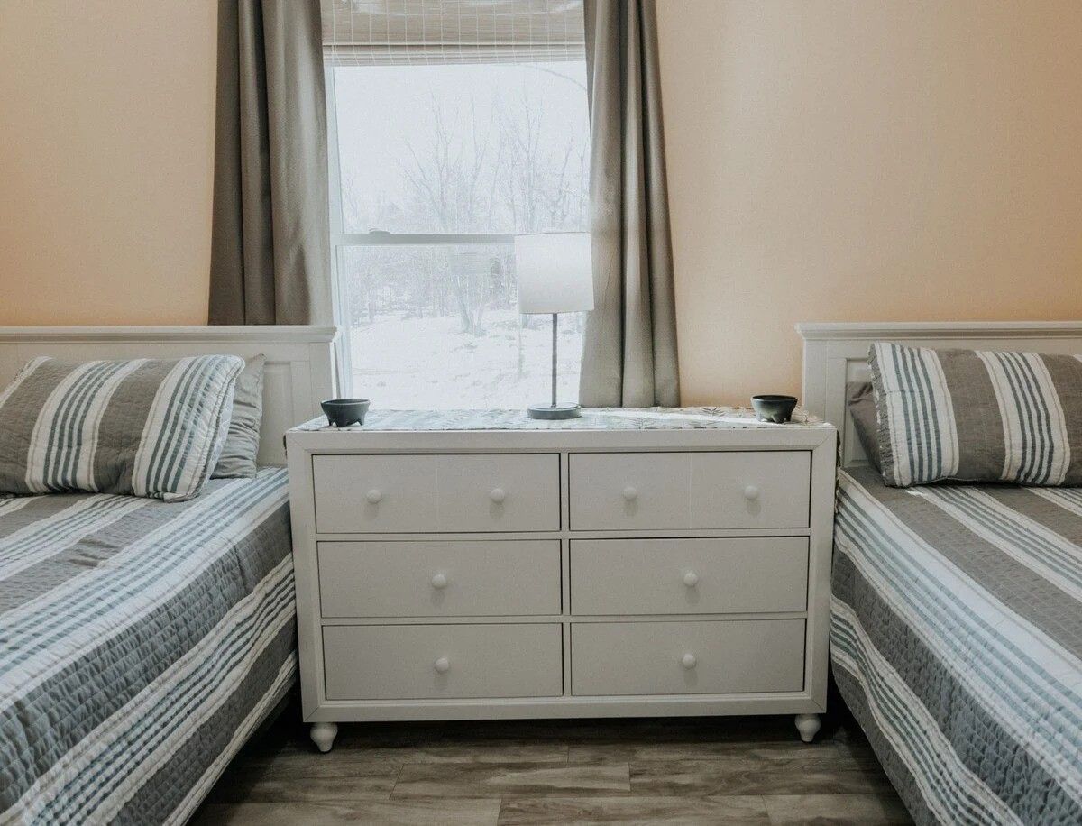 A bedroom with two beds, a nightstand, and a window with curtains.