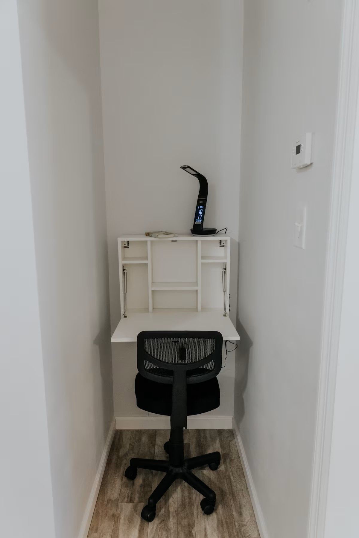 A small office space with a white desk, a black office chair, and a desk lamp.