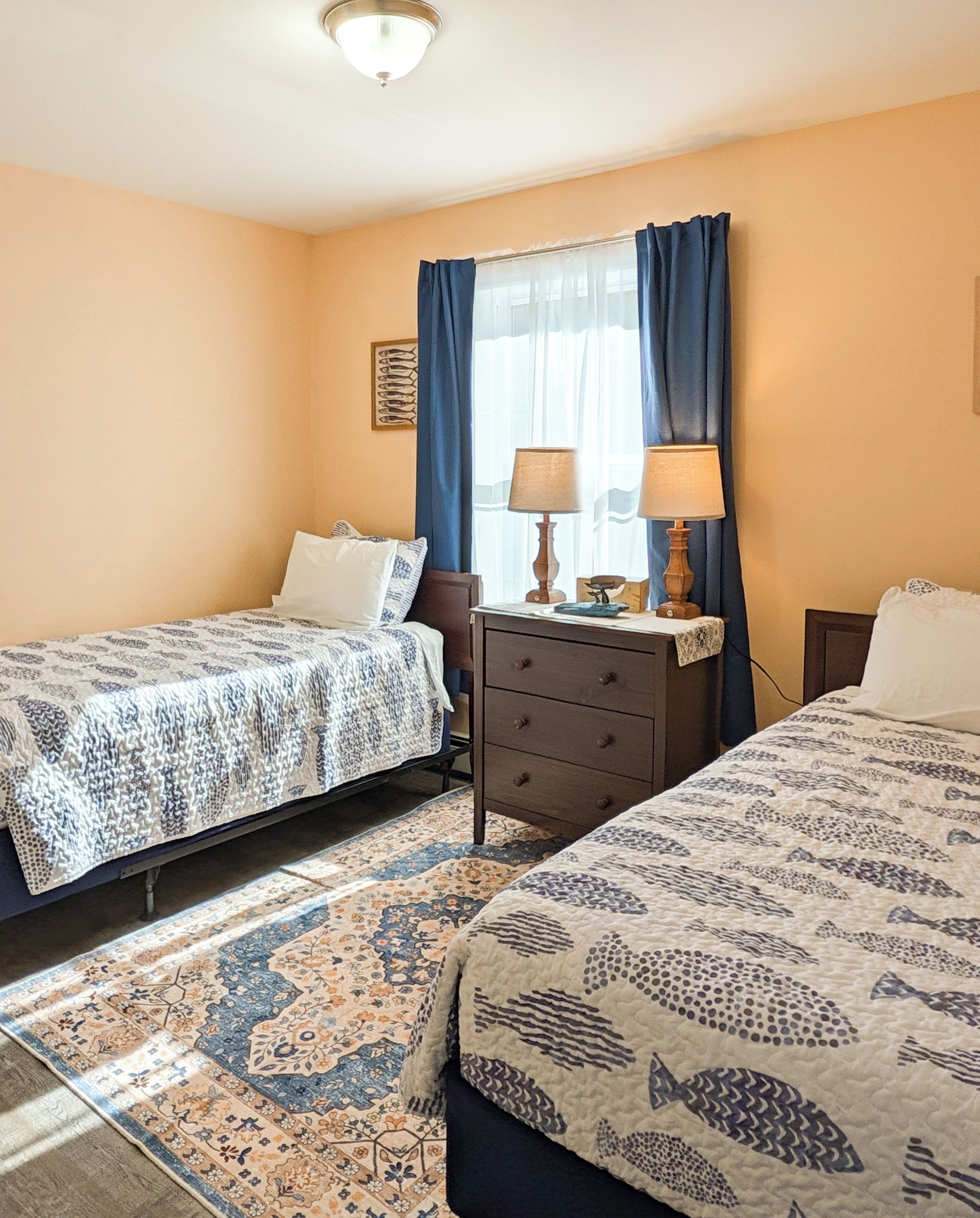 A hotel room with two beds, a nightstand, a dresser, and a window with curtains.