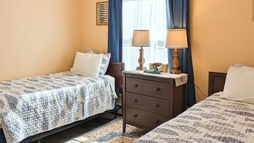 A hotel room with two beds, a nightstand, a dresser, and a window with curtains.