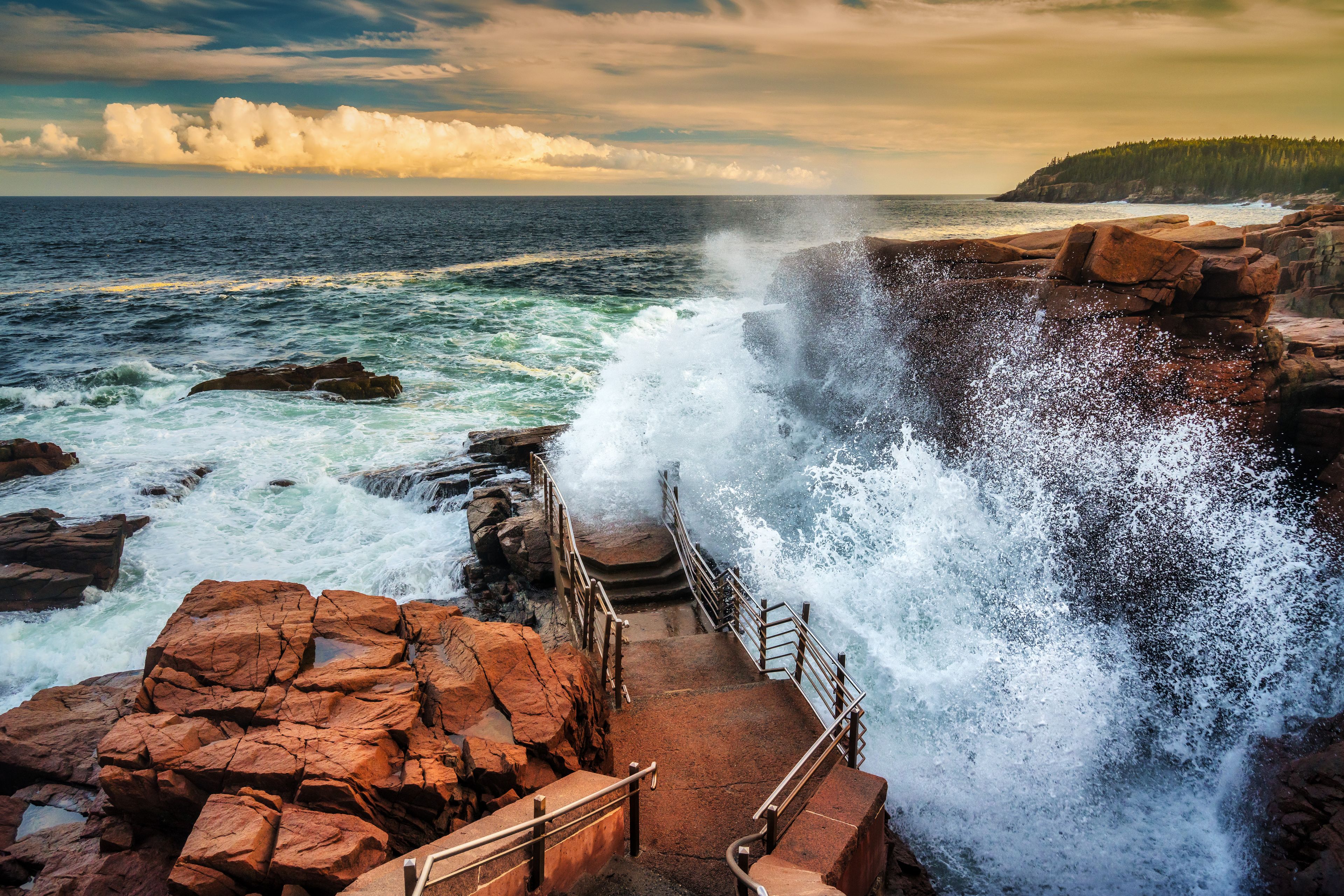 A coastal scene with a rocky shoreline, waves crashing against the rocks, and a staircase leading down to the water.
