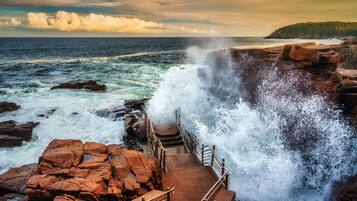 A coastal scene with a rocky shoreline, waves crashing against the rocks, and a staircase leading down to the water.