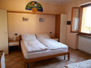 Ein Schlafzimmer mit einem Bett, einem Nachttisch, einer Kommode, einem Fenster und einem Wandventilator.