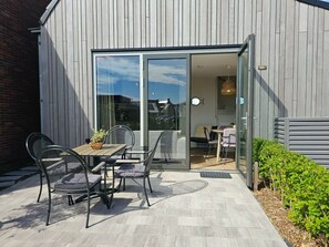Eine Außenpatio mit Tisch und Stühlen, eine Schiebetür zu einem Innenbereich und ein kleiner Garten.
