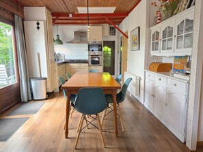 A dining area with a wooden table and chairs, a kitchen with white cabinets, and a view of the outdoors. - Ok03 Bungalow Rocky Docky (Oostkapelle)