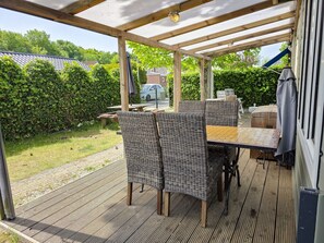 An outdoor patio with a wooden pergola, wicker furniture, and a view of a garden and a building in the background. - Ok03 Bungalow Rocky Docky (Oostkapelle)