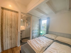 A bedroom with a bed, a bedside table with a lamp, a window with curtains, and a wooden door. - Ok03 Bungalow Rocky Docky (Oostkapelle)
