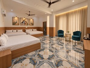 A hotel room with two beds, a ceiling fan, a marble-patterned floor, and a seating area with two chairs. - Alvora Resort (Chhata)