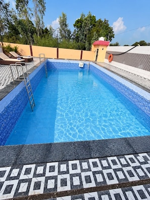 Una piscina rectangular con revestimiento de azulejos azules, rodeada por una terraza también de azulejos con un diseño geométrico.