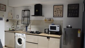 A compact kitchen with a washing machine, microwave, and a refrigerator. - London Studio_Hiranandani Estate_WiFi (Thane)