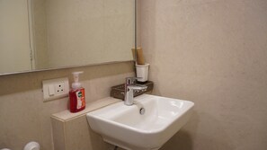 A bathroom with a white sink, a mirror, a soap dispenser, and a toothbrush holder. - London Studio_Hiranandani Estate_WiFi (Thane)