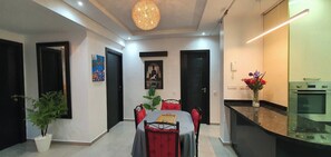 Ein modernes Wohnzimmer mit Esstisch, Stühlen, einer Kronleuchter und Kunstwerken an den Wänden.