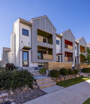 A modern multi-story residential building with a flat roof, a front entrance with steps, and a small front yard with a pathway and landscaping. - New! Monthly Midtown Bozeman Rental + Dogs Welcome (Bozeman)
