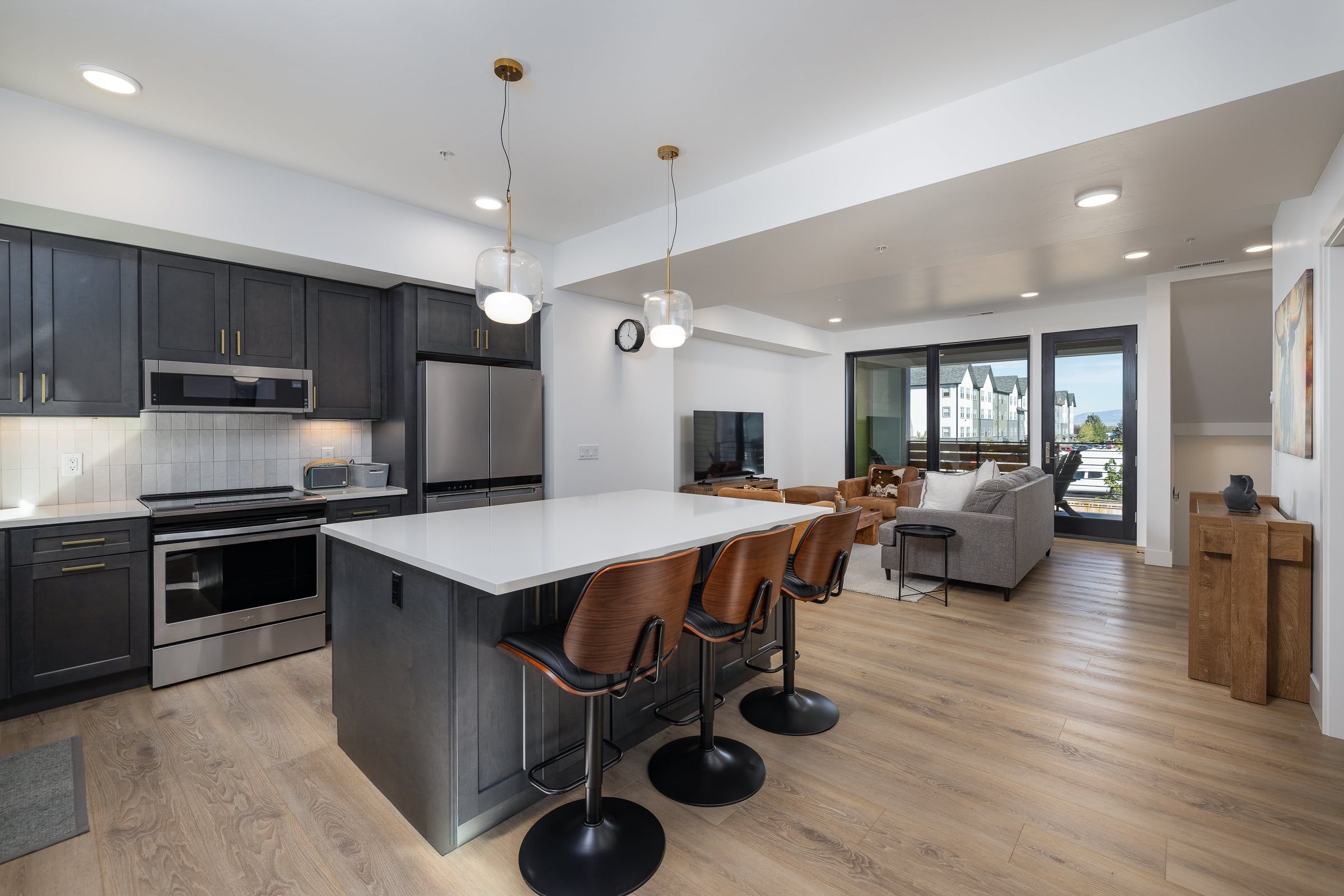 A modern kitchen with stainless steel appliances, a central island with bar stools, and a dining area with a view.