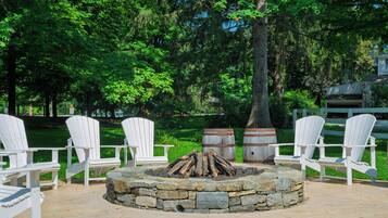 A stone fire pit surrounded by white Adirondack chairs in a park setting.