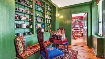 A room with green walls, a wooden bench, a chess table, and shelves with various items.