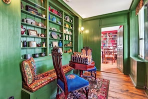 Une pièce aux murs verts, avec un banc en bois, une table d’échecs et des étagères remplies de divers objets.