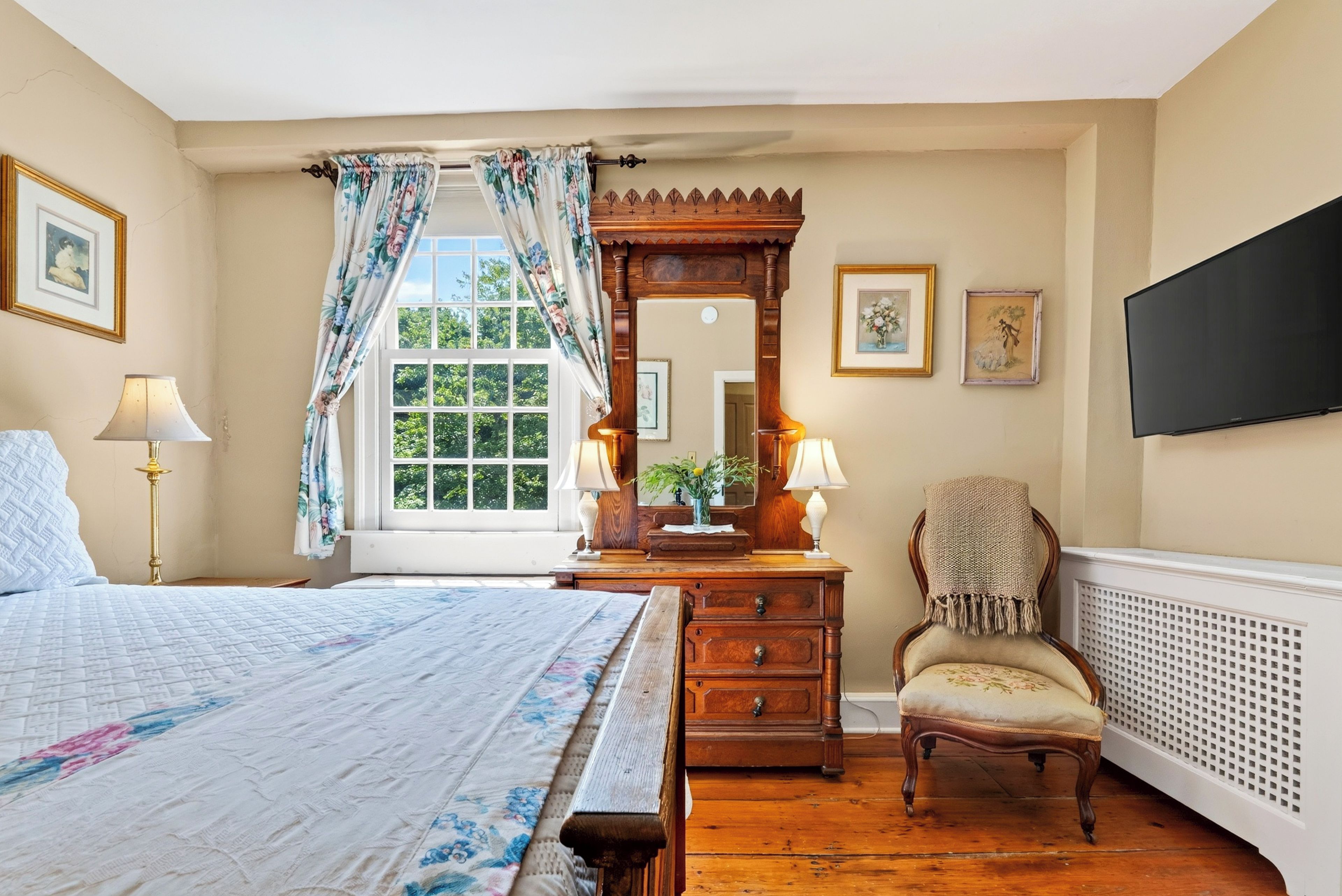 A bedroom with a large bed, a dresser, a chair, a mirror, and a window with curtains.