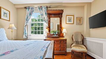 A bedroom with a large bed, a dresser, a chair, a mirror, and a window with curtains.
