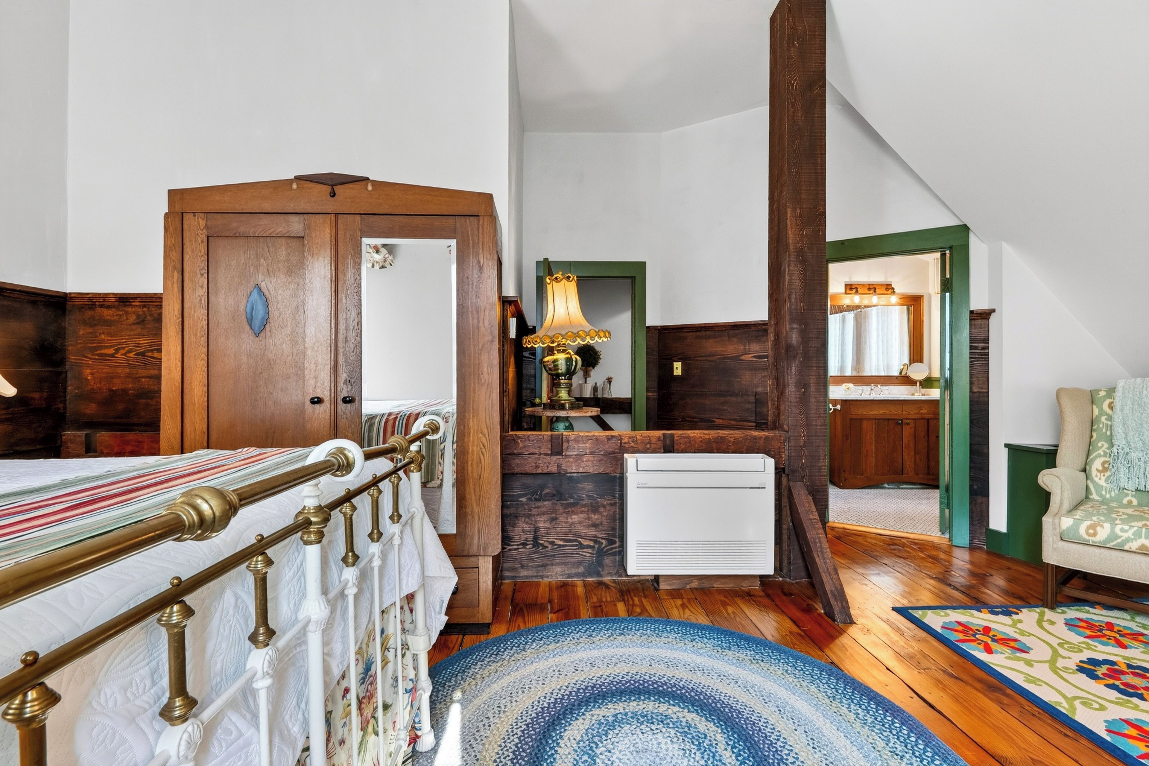 A bedroom with a bed, a dresser, a radiator, a mirror, and a chair.