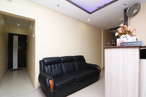 Zona de recepción con un sofá de cuero negro, mostrador de recepción y un ventilador de pared.