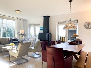 A modern living room with a sofa, chairs, a dining table, and a fireplace. - Ok32 Rural Holiday Home (Oostkapelle)