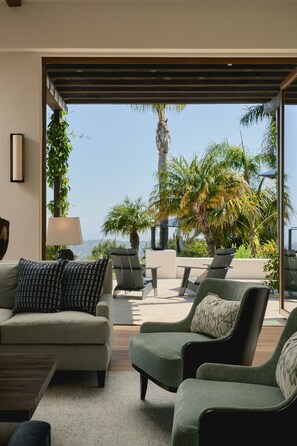 A modern living room with a sofa, chairs, and a view of a tropical garden through large windows. - Luxury Estate with Infinity Pool & Panoramic Views of Santa Barbara's Coast & Mountains (Santa Barbara)
