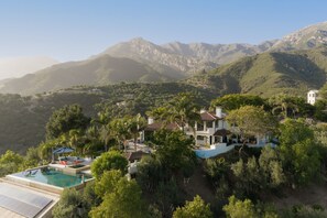 A hillside property with a swimming pool, multiple buildings, and a mountainous backdrop. - Luxury Estate with Infinity Pool & Panoramic Views of Santa Barbara's Coast & Mountains (Santa Barbara)