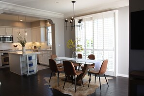 A modern kitchen with white cabinets, a central island, and a dining area with a glass table and brown chairs. - Darling Multi-Level Condo with Stunning Mountain Views & Close Proximity to The Beach! (Santa Barbara)