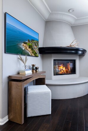 A living room with a fireplace, a mounted television, and a wooden console table with books. - Darling Multi-Level Condo with Stunning Mountain Views & Close Proximity to The Beach! (Santa Barbara)
