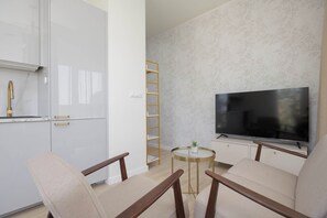 Ein modernes Wohnzimmer mit Flachbildfernseher, zwei Sesseln, einem kleinen runden Tisch und einer eingebauten Bücherreol.