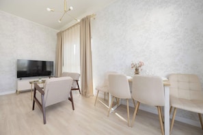 A modern living room with a flat-screen TV, a dining table with chairs, and a chandelier. - Warsaw | Zbąszyńska 4 | Spacious Apartment | Balcony (Warszawa)