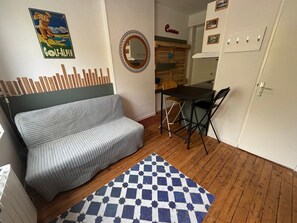 A compact living space with a sofa, a small dining table, a foldable chair, a checkered rug, a mirror, and a kitchen area. - The Little Golfer - 17m² studio Arras city center (Arras)