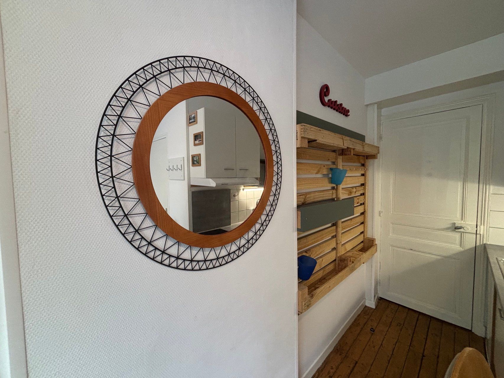 A room with a circular mirror on the wall, a wooden slatted shelf, and a door with a sign above it.