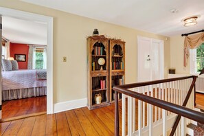 A room with a wooden floor, a bookshelf, a bed with a patterned bedspread, and a door with a window. - Library + Sunroom + Dining for 8 | Ensuite Baths + Gardens | Preston House (74) (Dover Plains)