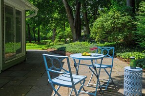 An outdoor patio with two blue metal chairs and a small round table, surrounded by lush greenery and trees. - Library + Sunroom + Dining for 8 | Ensuite Baths + Gardens | Preston House (74) (Dover Plains)