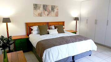 Een slaapkamer met een bed, twee nachtkastjes, een dressoir, een groene kast, een houten bankje, een bloempot en een kledingkast.
