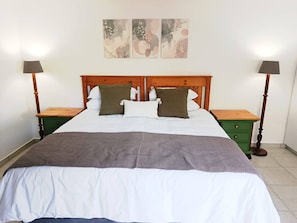 Ein Doppelbett mit Holz-Kopfteil, zwei Nachttische, eine grüne Schubladenkommode und eine graue Tagesdecke.