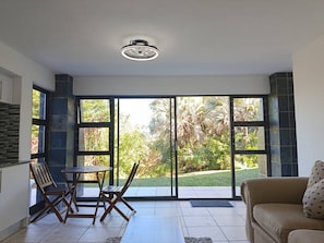 A room with a sliding glass door leading to a garden, a wooden table with chairs, and a sofa. - The Tee Box - Stay, Relax & Unwind (Southbroom)